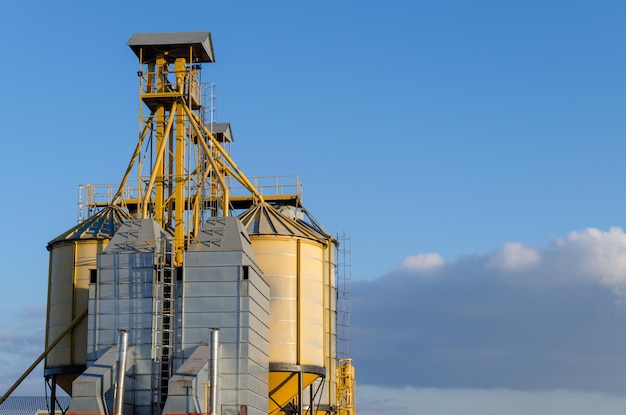 A large modern plant for the storage and processing of grain\
crops view of the granary on a sunny day large iron barrels of\
grain against the sky end of harvest season