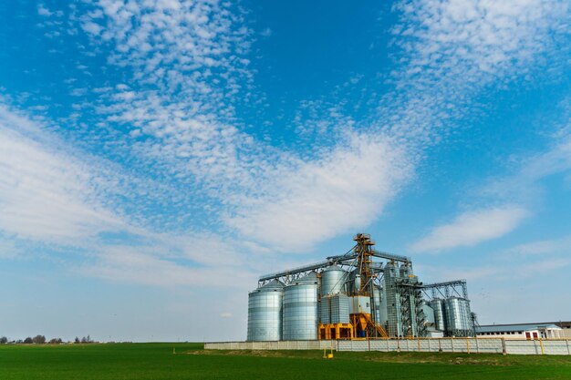 A large modern plant for the storage and processing of grain\
crops view of the granary on a sunny day large iron barrels of\
grain silver silos on agro manufacturing plant for processing and\
drying