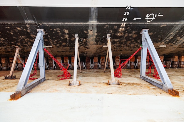 A large motor yacht is in dry dock resting on wooden blocks and supported by metal piers