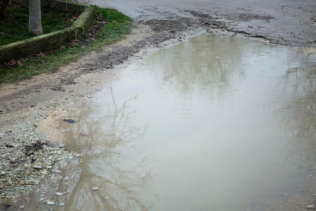 A large muddy puddle on the road on a rainy day Closeup Hopelessness and dirt Space for text