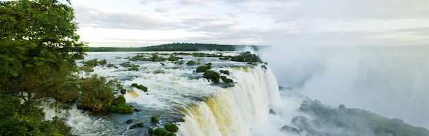 Large nature panorama of Iguacu (Iguazu) waterfall cascade on border of Brazil and Argentina. Amazing view of falls Cataratas in bright Sunny weather. Concept of travel. Copyright space for site