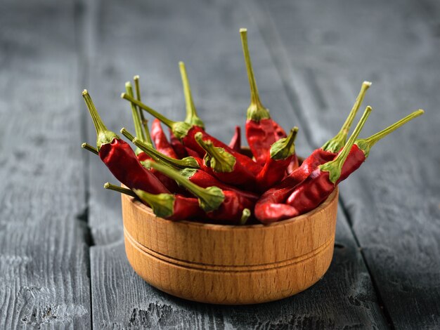 A large number of dried chili peppers in a wooden bowl on a rustic table.