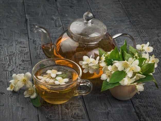 A large number of jasmine flowers and a glass teapot with flower tea on a wooden table.