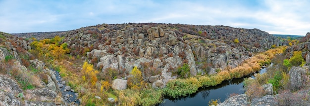 Большое количество каменных минералов, покрытых растительностью, лежащих над небольшой речкой в живописной Украине.
