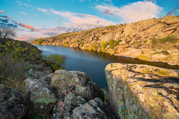 a large number of stone minerals covered with vegetation lying over a small river in picturesque ukraine