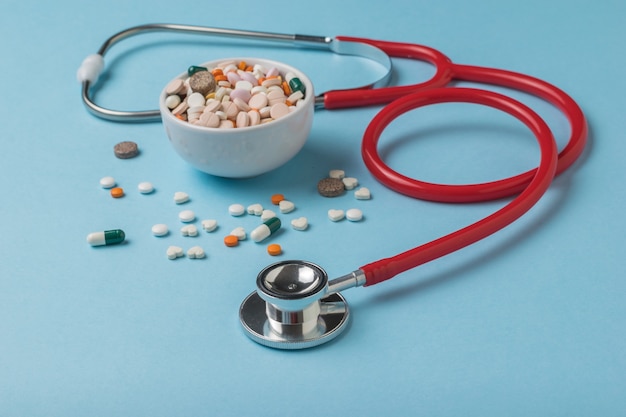 A large number of tablets and capsules and a red stethoscope on a blue background.