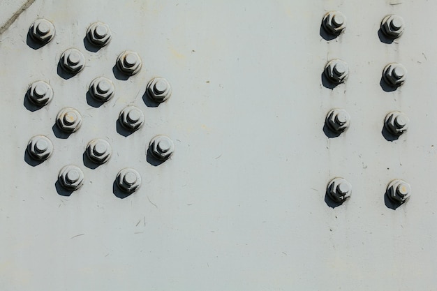 Large nuts and bolts on gray steel plate of rail bridge, lit by bright sun. Abstract industrial background.