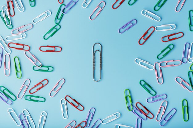 A large paper clip surrounded by small colored paper clips on a blue background