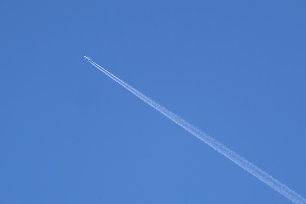 Большой пассажирский самолет летит высоко в ясном безоблачном голубом небе, оставляя длинный белый след