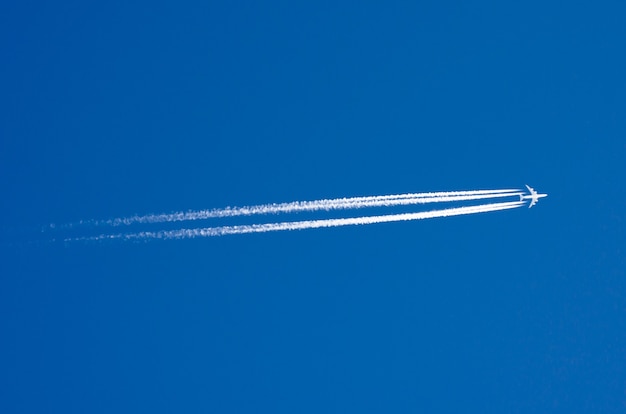 Large passenger liner and trail from an airplane in a blue sky.