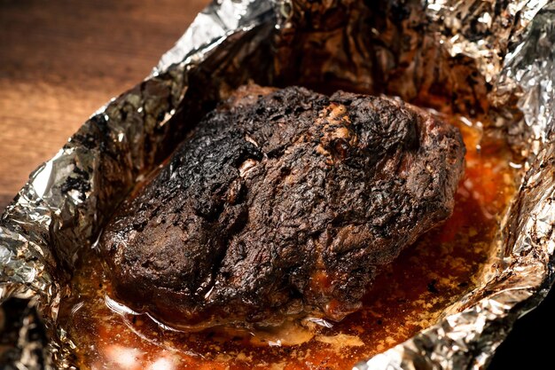 A large piece of baked meat with spices wrapped in foil in the oven