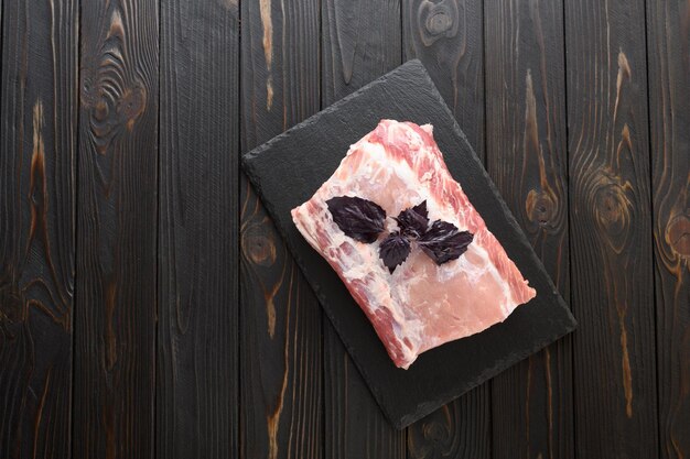 A large piece of pork loin with basil on a rustic dark background