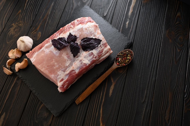 A large piece of pork loin with basil on a rustic dark background