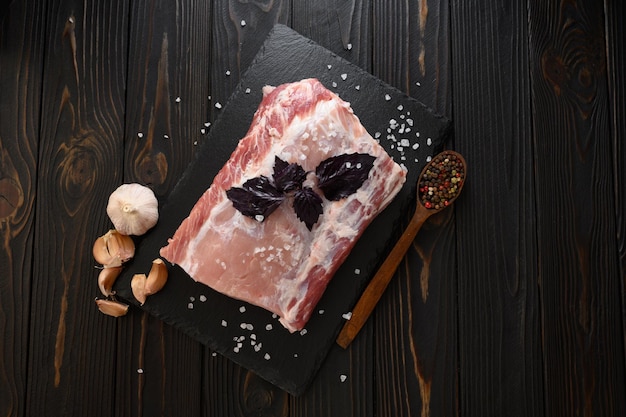 A large piece of pork loin with basil on a rustic dark background