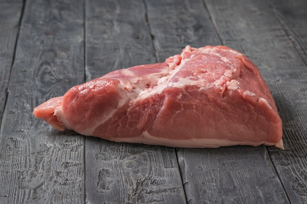 A large piece of pork meat on a black wooden table. Ingredients for cooking meat dishes.