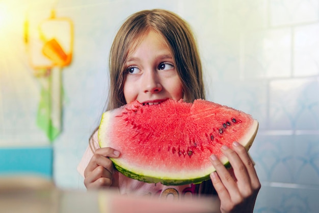 青い背景の上の小さな女の子の手に熟した赤いスイカの大きな部分小さな女の子はスイカのスライスを保持し、彼を食べる