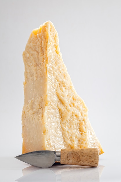 Large pies of parmesan cheese with small cheese knife on white background, vertical composition