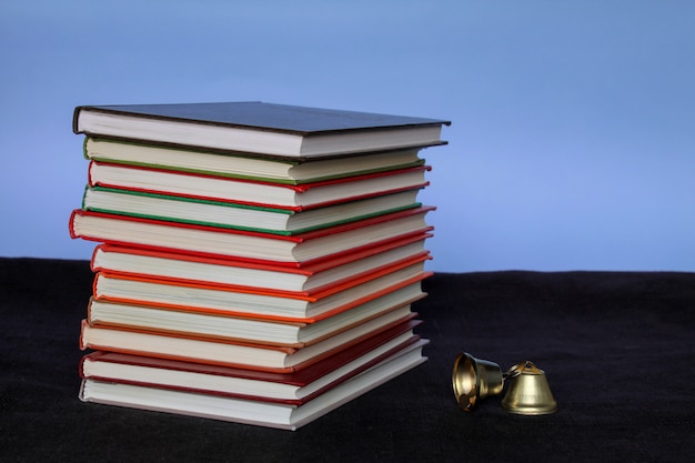 A large pile of books and a bell side view on a blue background