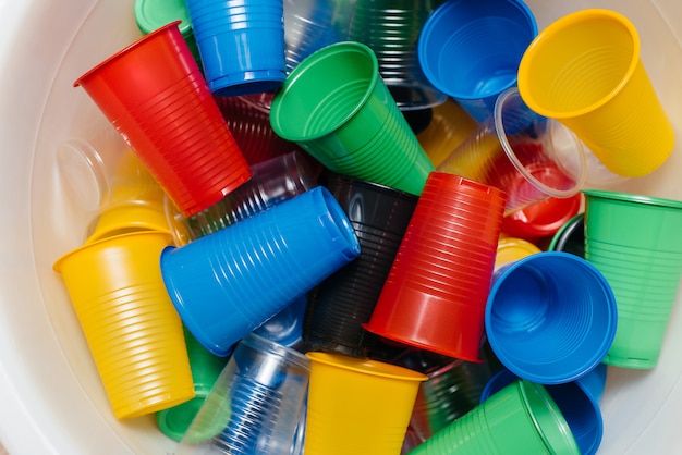 A large pile of multicolored plastic cups scattered on the floor. Pollution of the environment by human waste.