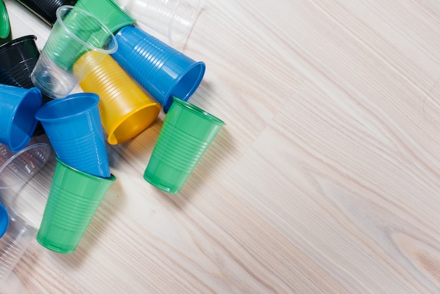 A large pile of multicolored plastic cups scattered on the floor with free space. Pollution of the environment by human waste