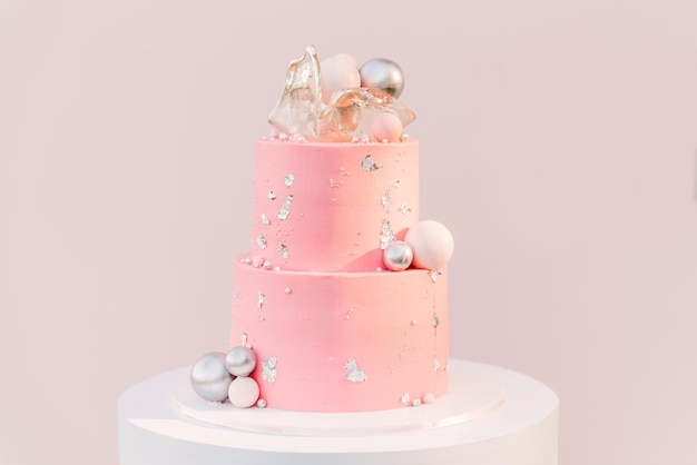 背景に銀の風船のピンクの写真ゾーンを持つ大きなピンクのケーキ。風船で飾られたパーティー