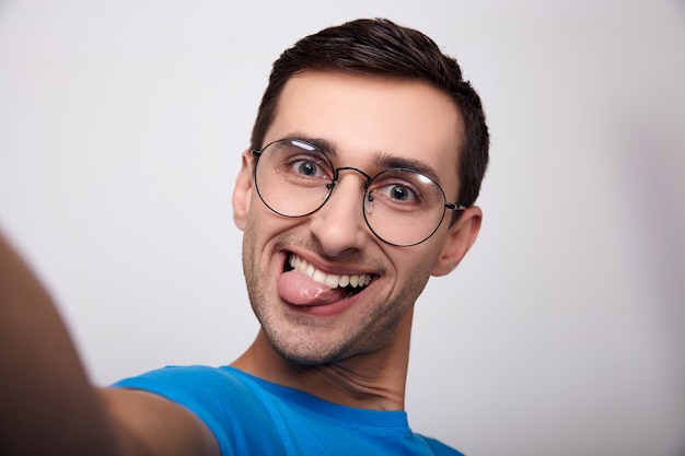 A large plan portrait of a young man with glasses with his tongue stuck out.