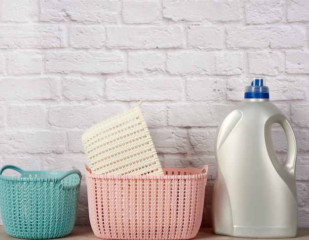Large plastic bottle with liquid detergent and a stack of baskets on white brick wall