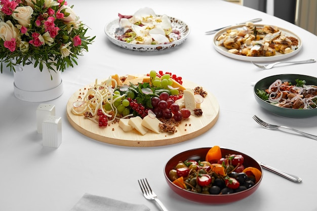 A large plate of assorted cheeses with grapes and nuts surrounded by other snacks and flowers on a banquet table, various cheeses with fruits and other snacks, celebration.