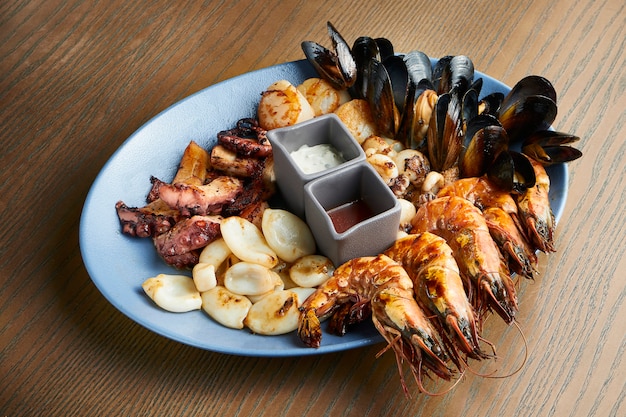 A large plate of fried seafood - squid, octopus, mussels, scallops, shrimp. Assorted seafood on a ceramic plate on a wooden surface. Film effect during post. Soft focus