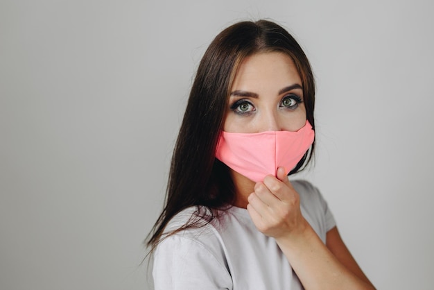 A large portrait of a girl with eye makeup covers her mouth with a mask and looks at the camera