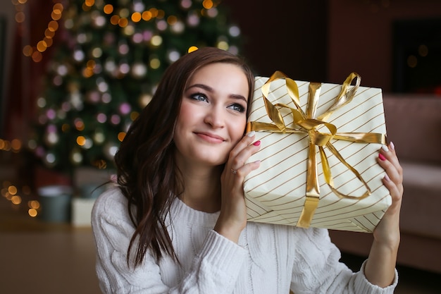 Large portrait of a happy sweet smiling woman with a Christmas gift box near a tree