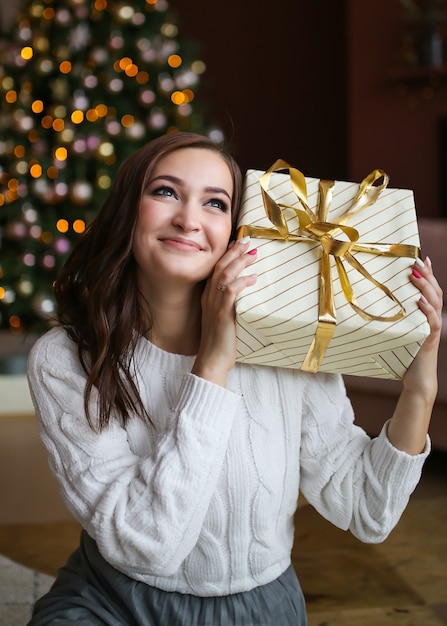 Large portrait of a happy sweet smiling woman with a gift box near a Christmas tree