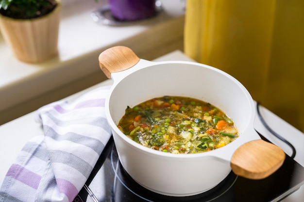 Large pot with vegetable soup minestrone at the kitchen table ready to be served to diners