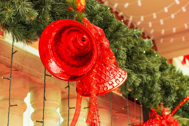 Большие красные рождественские колокольчики с бантами, огни, зеленые ветки елки крупным планом. Новый год 2021 и Рождество, новогоднее настроение, новогодние украшения