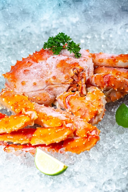 large red Kamchatka crab, lies on ice, with claws, cherry, slices of lemon and lime are sliced round