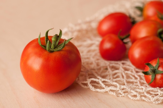 A large red tomato with a green tail on the background of a string bag with small tomatoes