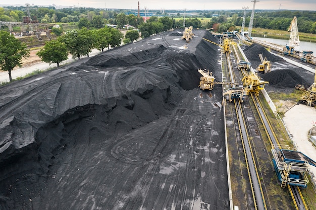 Large reserves of coal at a power plant, many cranes unloading\
coal, a lot of coal, top view