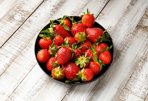 Large ripe juicy berries of organic strawberries in a black round plate on a light wooden background