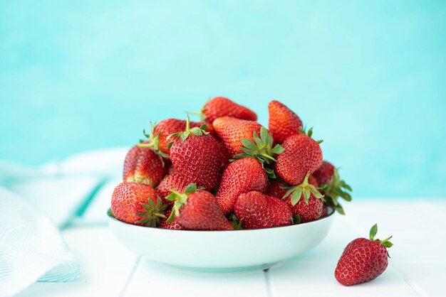 Photo large ripe sweet strawberries in a ceramic plate on a turquoise background