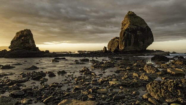 Photo a large rock formation is in the water with a sunset behind it