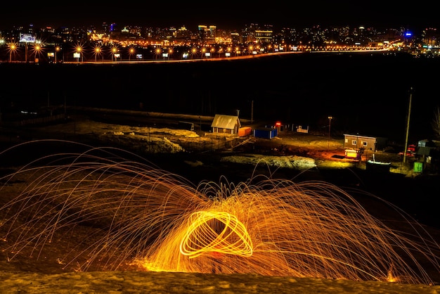 Большие круглые горящие фейерверки сверкают из горящей стальной шерсти, освещающей ночной город.