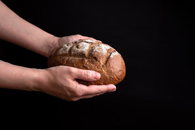 Large round loaf of rye bread in female hands