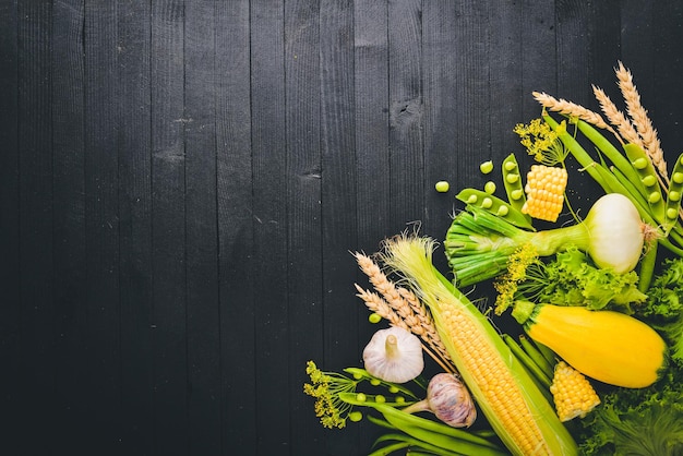 A large selection of raw fresh vegetables Corn zucchini lettuce greens On a black wooden background Top view Free space for your text