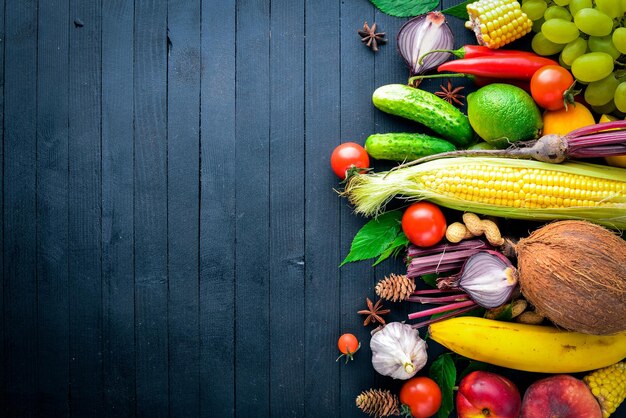 Large selection of raw vegetables and fruits on a black wooden table Free space for your text Top view