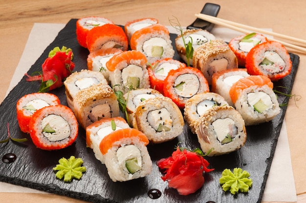 A large set of sushi rolls on a black stone plate