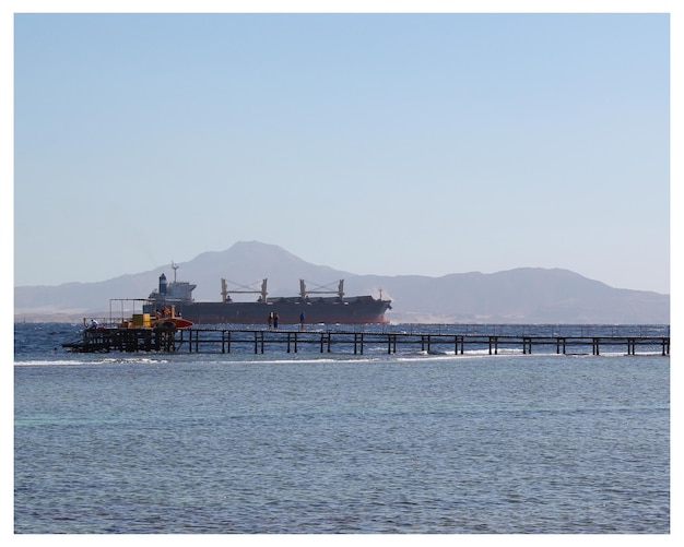 A large ship is docked in the ocean with a mountain in the background.