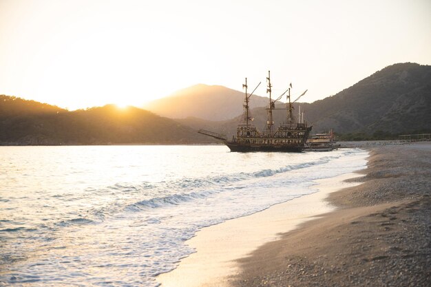 A large ship is docked at the seashore at sunset and beautiful mountains