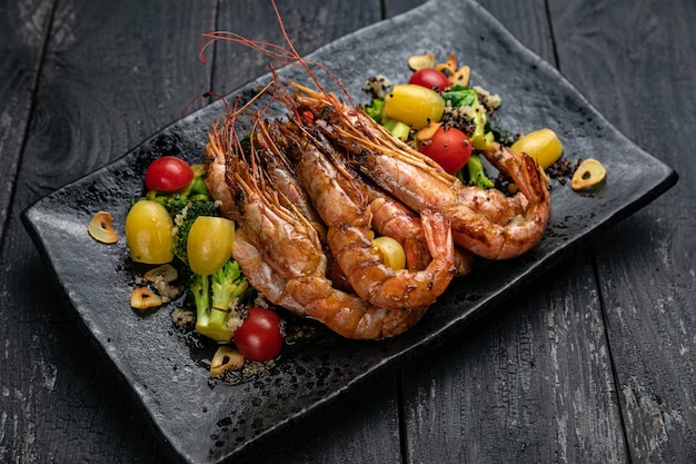 Photo large shrimp on a dark plate with vegetables