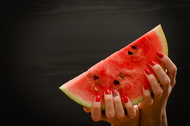 Large slice of ripe watermelon in female hands on a black ,  space for text