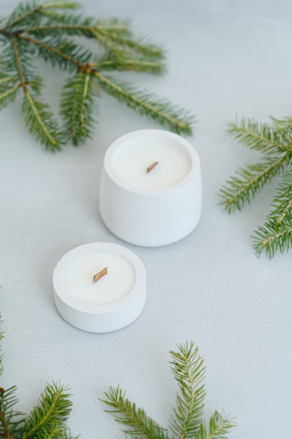 Large and Small Soy Scented Candle on Light Background Among Christmas Tree Branches